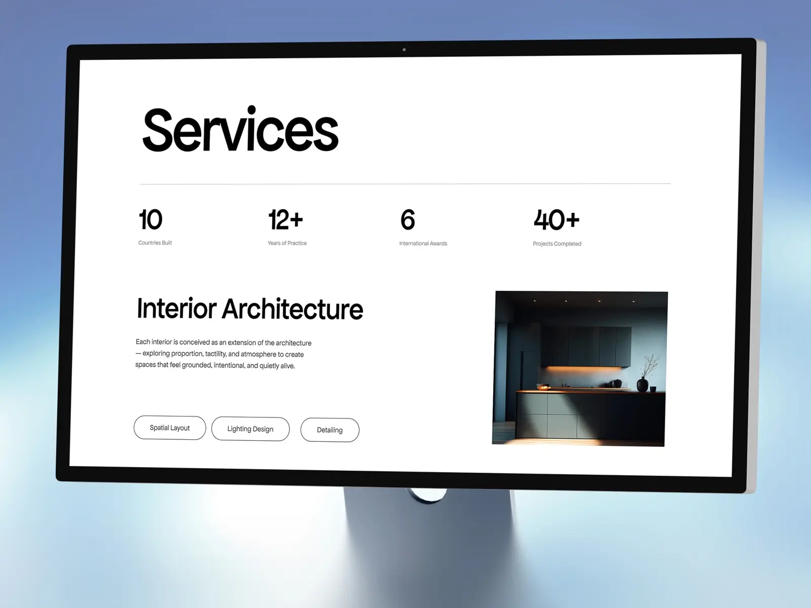 Monitor displaying a sleek webpage titled 'Services' with key statistics: 10 countries built, 12+ years of practice, 6 awards, 40+ projects. Focus on 'Interior Architecture' with a modern, dimly lit kitchen image, evoking a sense of elegance and professionalism.